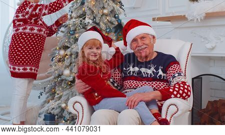 Granddaughter Exhcanging Christmas Gift Present Boxes With Amazed Happy Senior Grandfather At Home. 