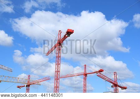 Construction Of A Modern Residential Complex. Silhouette Of Lifting Cranes Against Natural Blue Sky 