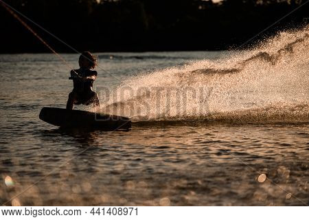 Woman Wakeboarder Holds Taut Cable And Standing On Wakeboard On The Surface Of The Water
