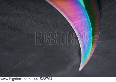The Curved Sharp Blade Of The Kerambit Dagger Is A Gradient Rainbow Color On A Dark Background.