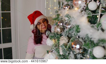 Woman Admiring Christmas Tree. A Beautiful Brunette In A New Years Hat, Admiring The Christmas Tree.