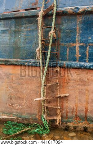 A Homemade Ladder Made Of Ropes And Planks Hangs From An Abandoned Ship