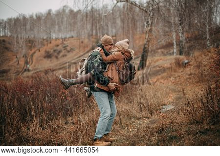 A Loving Couple With Hiking Backpacks Walks In The Fall In Nature. A Girl In A Beige Hat, Brown Jack