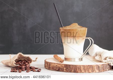 Cup Of Dalgona Coffee On Wooden Table With Bag Of Natural Coffee Beans And Cinnamon Stick