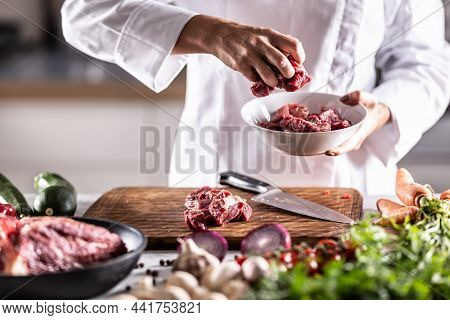 Detail Of Red Meat Chunks Put Into A White Bowl On A Meal Preparation Table Full Of Ingedients.
