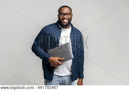 Smiling Young African-american Male Entrepreneur Stands In Studio Isolated On Gray And Carrying Tren