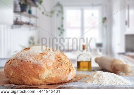 Freshly Baked Artisan Bread In Baking Paper On Table With Ingredients And Rolling Pin With Kitchen B