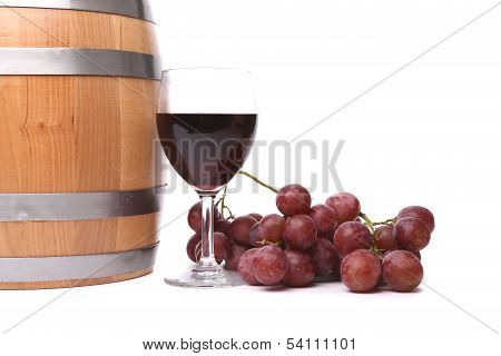A glass of red wine with grapes and barrel.