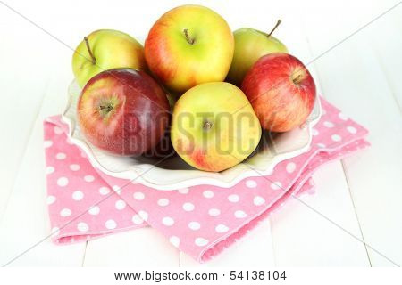 Juicy apples on plate on white wooden table