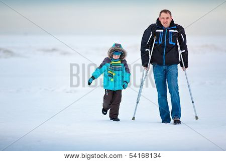 Man with crutches and his little son outdoors