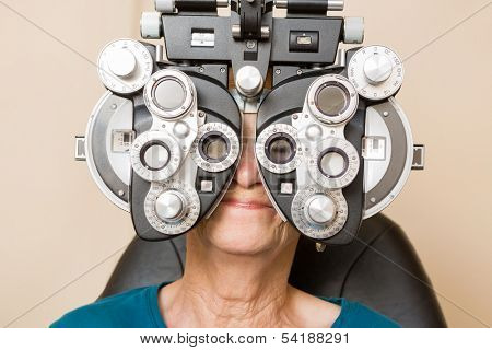 Senior woman looking through phoropter during eye exam