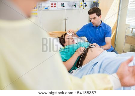 Caring man wiping exhausted pregnant woman's forehead in hospital room