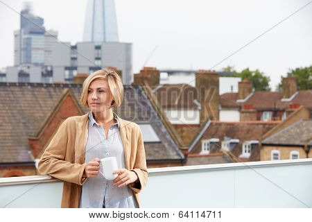 Young Woman Relaxing On Roof Terrace With Cup Of Coffee