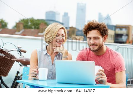 Young Couple Sitting On Roof Terrace Using Laptop