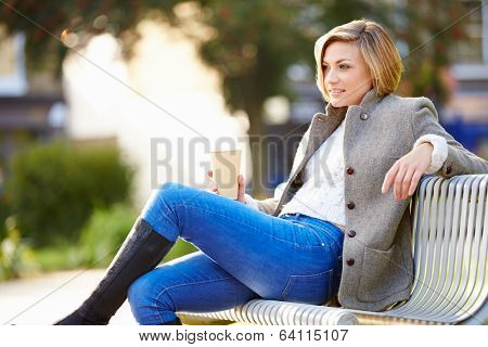 Woman Relaxing On Park Bench With Takeaway Coffee