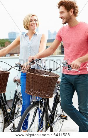 Couple Pushing Bikes With City Skyline In Background