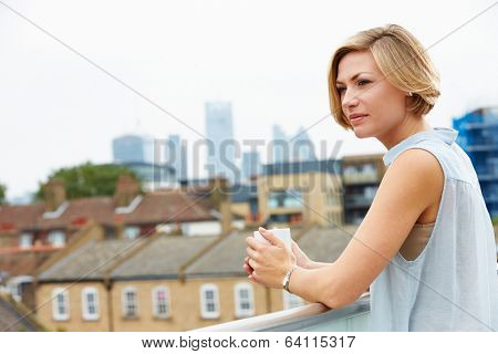 Young Woman Relaxing On Roof Terrace With Cup Of Coffee