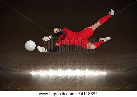 Fit goal keeper jumping up against large football stadium with spotlights at night