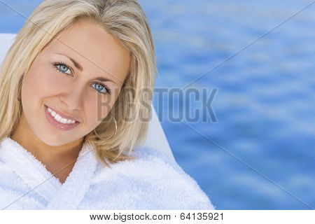 Beautiful blonde girl young woman in white spa robe with natural blue water background