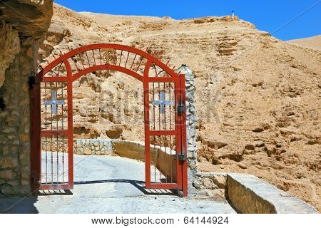 Decorative red gate with a cross on a mountain road going to the temple. Wadi Kelt near Jerusalem