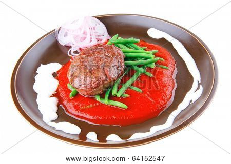 pork medallion served on tomato sauce with green peas on dark plate isolated on white background