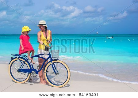 Happy mother and her daughter riding bicycles on a tropical beach