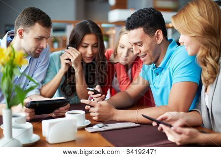 Portrait of teenage friends using modern gadgets while sitting in cafe