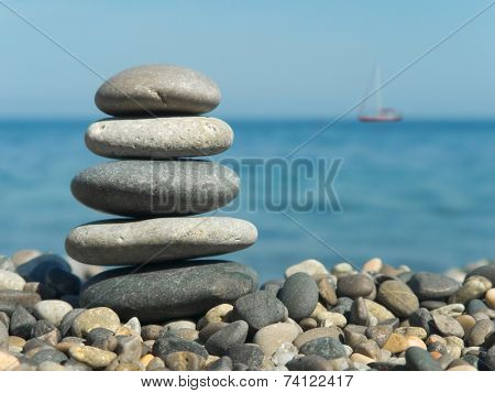 Stack of stones on beach and yacht in sea