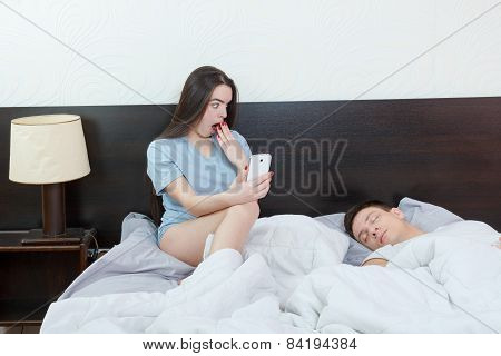 Young Shocked Woman Looking Phone While Man Is Sleeping Soundly