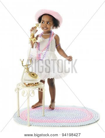 An adorable two year old diva standing in her petticoat and pearls and chatting on a fancy French phone.  On a white background.