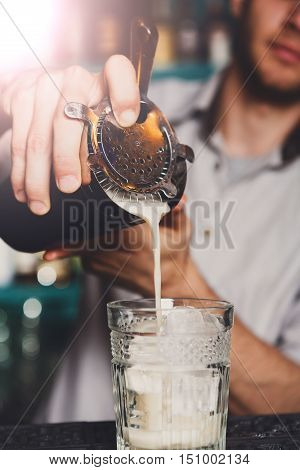 Barman's hands in bar interior making alcohol shot cocktail. Professional bartender at work in bar pouring coconut syrup into glass. Party time in night club. Service industry occupation