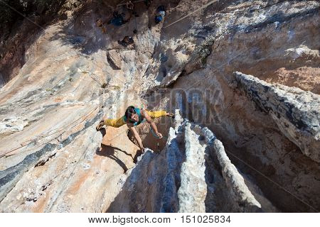 Top View of Mature Male Extreme Climber in bright sportive Clothing hanging on unusual shaped Rock Daylight Outdoors orange and blue Colors of Stone Texture