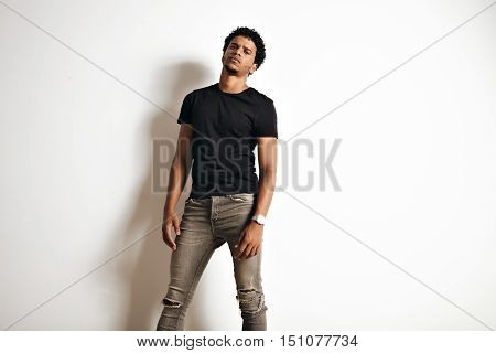 Sexy sensual gloomy looking African American model in a blank black t-shirt and skinny jeans against a white wall background