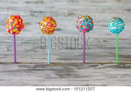 Four cake pops. Bright candies on wooden background. Go eat some sweets. Choice of taste.
