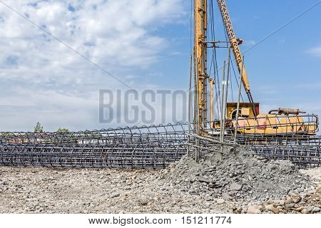 Basic profile made of bended and tied reinforcing rod in a round shape. Pile driving machine with big auger equipment for drilling into the ground.
