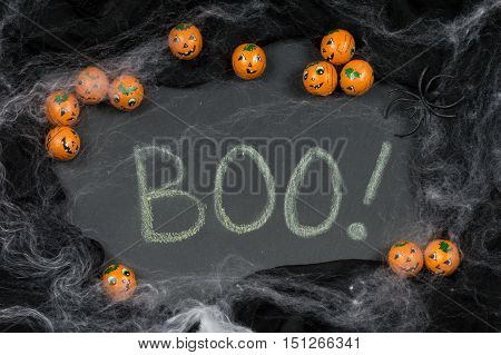 Boo! Written in chalk on slate framed with Halloween candy Jack-o-lanterns spider and spooky cobwebs.