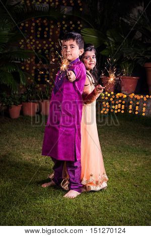 indian cute Boy and girl in traditional wear playing with sparklers or fulzadi or phuljhadi on diwali night