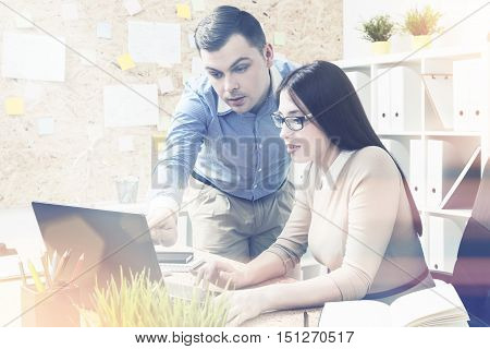 Woman in glasses working at computer man standing next to her and showing something on scren. Office. Concept of work. Toned image