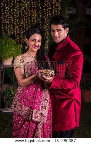 Indian young Woman holding a diya and husband standing behind, indian young couple celebrating diwali with diya in hand