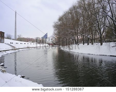 Winter cityscape with not frozen Iset River. Yekaterinburg. December. Trees are reflected in water. On a background buildings of circus the unfinished house and a television tower are visible. In Yekaterinburg in 2018 will pass the soccer World Cup
