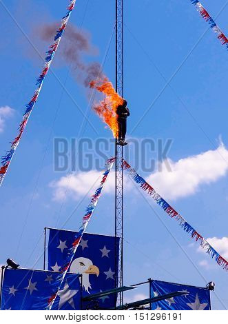A Daredevil Fire Diver preparing to jump off a high dive platform into a pool of water. Stuntman dressed in black fire protective suite. A very dangerous and extreme yet exciting athletic sport stunt.