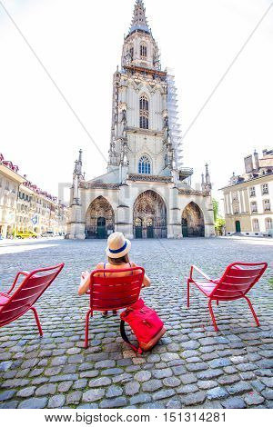 Young female tourist sitting on the red public chairs on Munster square in the old town of Bern city in Switzerland