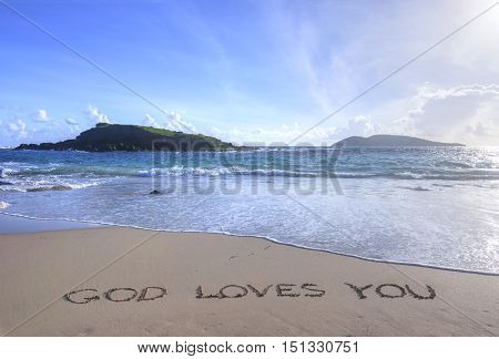 Message in sand reads God Loves You on tropical Caribbean beach of Isla Culebra in Puerto Rico with small islands in background