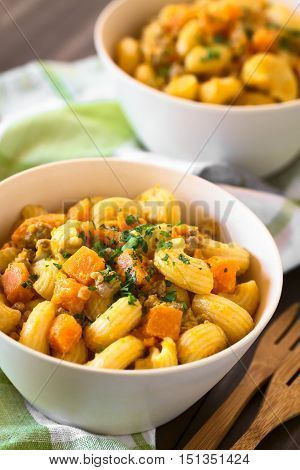 Macaroni pasta with creamy pumpkin and mincemeat sauce garnished with parsley served in white bowls photographed with natural light (Selective Focus Focus in the middle of the first dish)