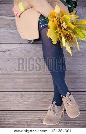 Top view on woman's hands holding beautiful bunch of yellow marple leaves. Young woman with bouquet of autumn leaves sitting on wooden bridge in park. autumn thanksgivining and lifestyle concept