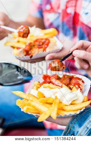 Man and woman eating german specialty Currywurst and french fries on scooter