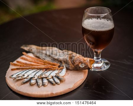 Glass of beer and assorted dried fish on a cooking sheet traditional beer snack. Black wooden background.