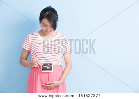 pregnant woman take ultrasound picture and smile isolated on bluebackground asian
