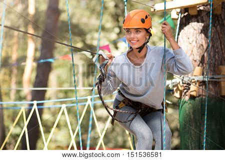 On the way to adventures. Pleasant determined cheerful woman holding the ropes and preparing to start moving forwards while having fun in the rope park