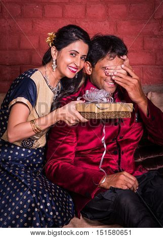 Indian wife surprising husband with a gift on diwali or anniversary or birthday, surprise gift concept and indian people or couple